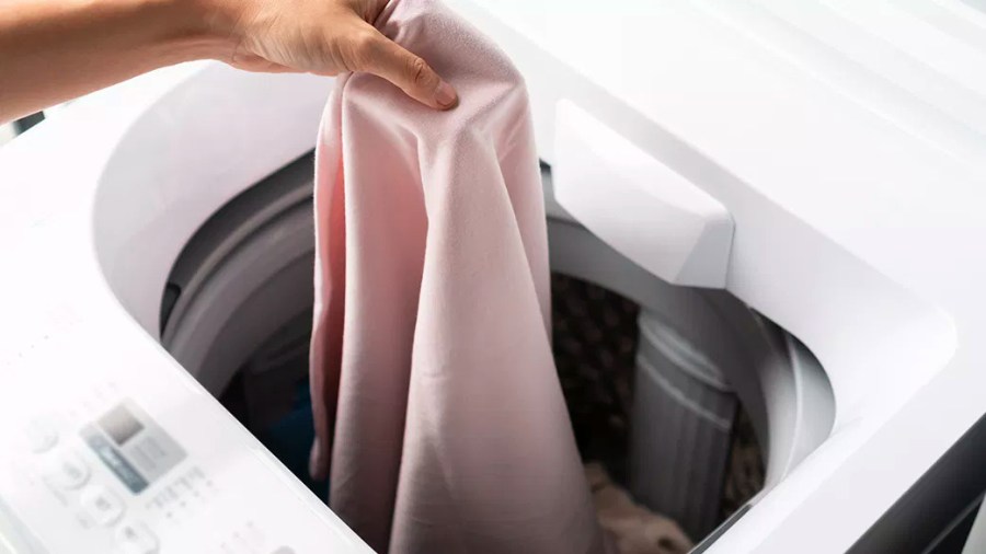 Person placing a pink garment into a washing machine