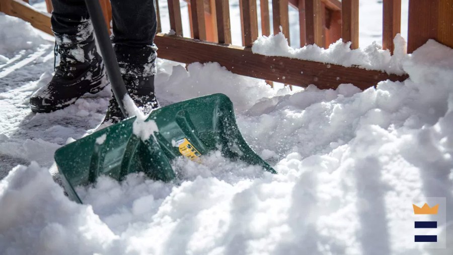 Person using a snow shovel with a green blade to remove snow on their deck