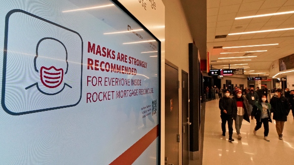 Fans wearing face masks walk past a sign recommending masks before an NBA basketball game