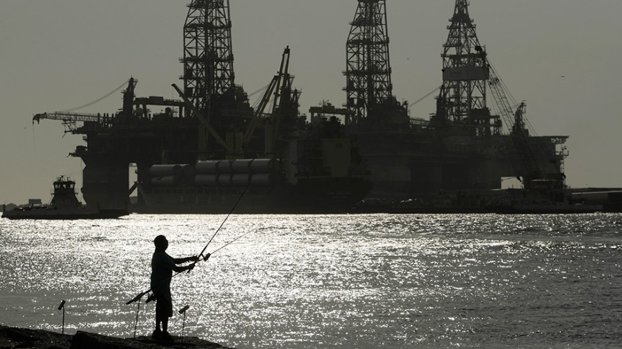 A person fishes with an oil drilling rig in the background.