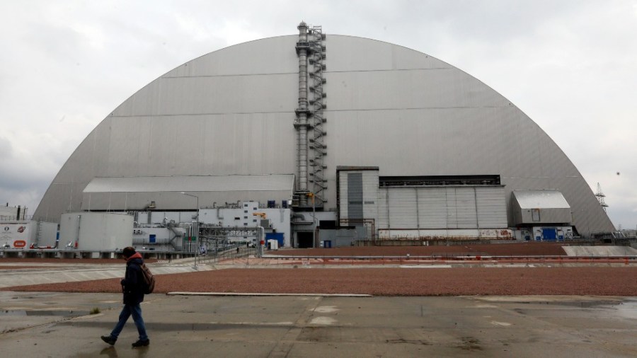 A man walks past a shelter covering the exploded reactor at the Chernobyl nuclear plant, in Chernobyl, Ukraine