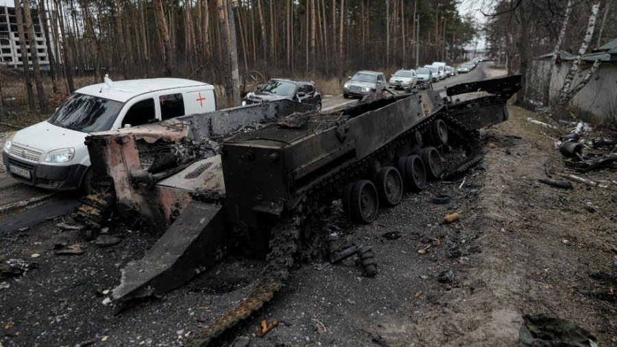 Cars drive past a destroyed Russian tank as a convoy of vehicles evacuating civilians leaves Irpin, on the outskirts of Kyiv