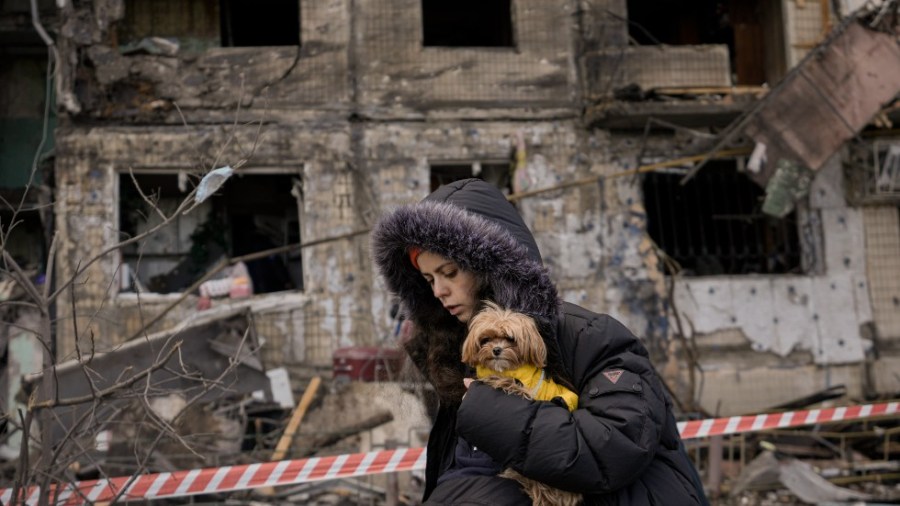 A woman holding a small dog walks in front of an apartment in a block which was destroyed by an artillery strike in Kyiv, Ukraine