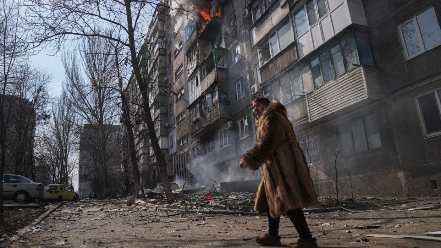 A woman walks past a burning apartment building after shelling in Mariupol, Ukraine