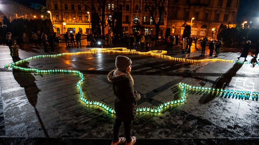 A girl stands in front of lit candles forming the shape of Ukraine's map