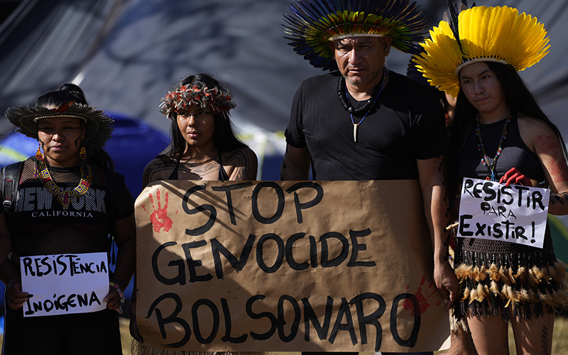 A Tembe Indigenous family carries posters written in Portuguese that read "Indigenous Resistance," left, and "Resist to Exist," right, with "Stop Genocide Bolsonaro" center