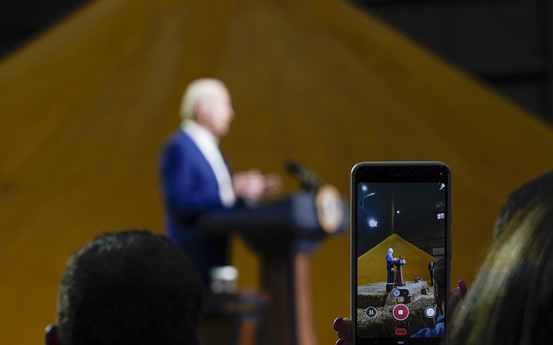 An attendee records a video with her phone as President Biden speaks in the background