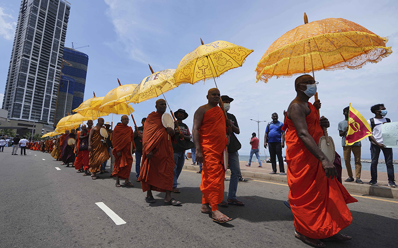 Sri Lankan Buddhist monks, wearing orange and holding golden umbrellas, arrive at the ongoing protest site outside the president's office