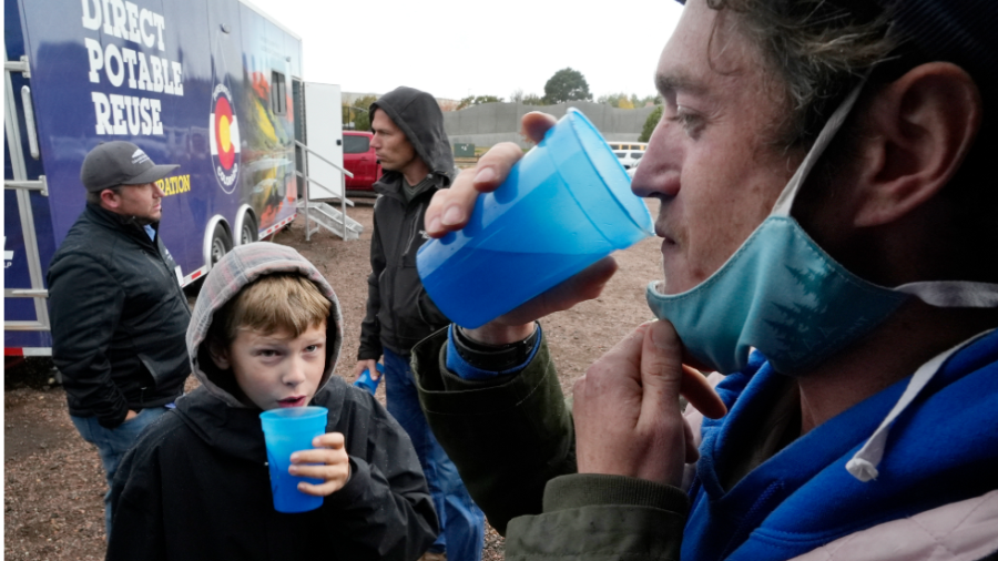 A man and child drink water from blue cups near a van that reads "Direct Potable Reuse"