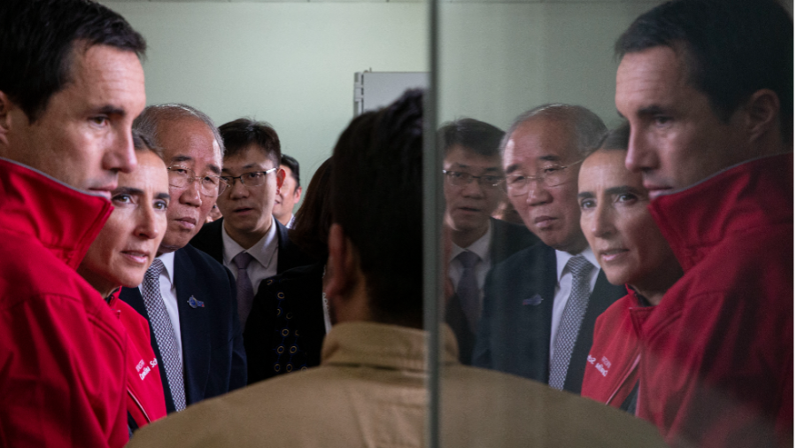 The faces of government officials from Chile and China are reflected in glass.