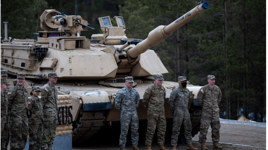 U.S. soldiers stand in front of a tank with arms crossed behind their backs