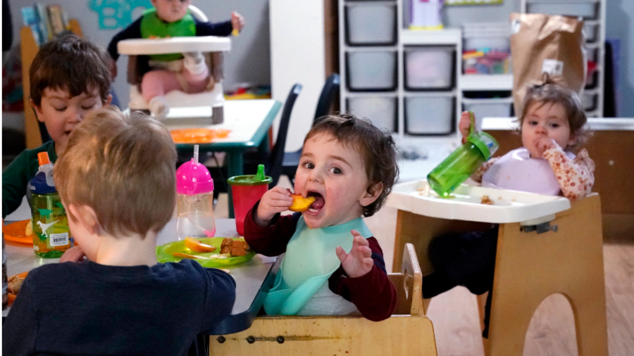 Toddlers in a day care, sitting in high chairs eating fruit.