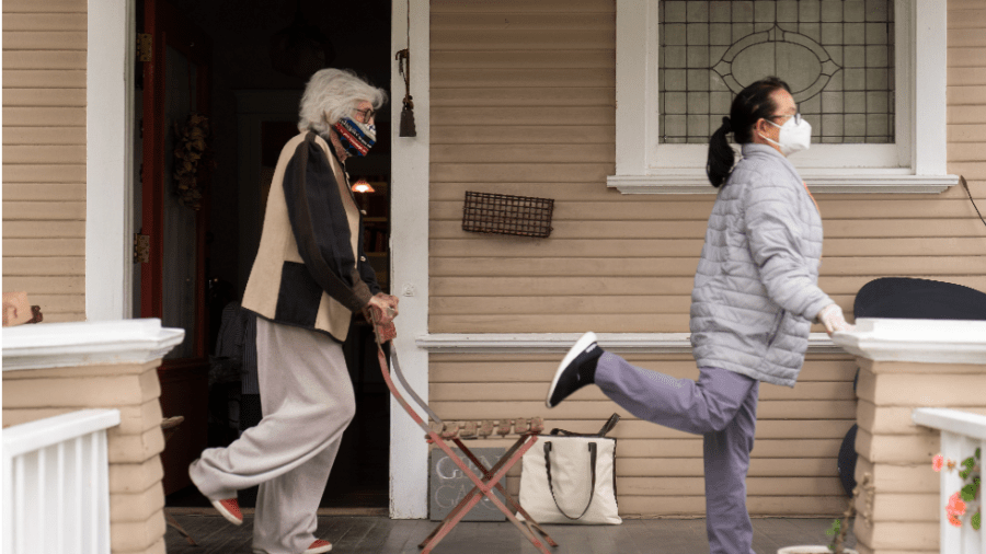 A woman and a home health aide exercise on a front porch.