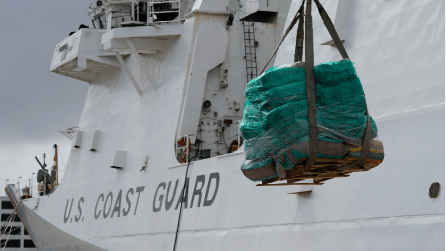 A pallet covered in green tarp is lifted onto a Coast Guard ship.