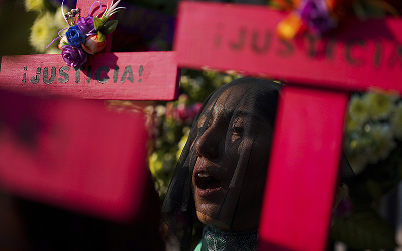 A demonstrator in a black veil shouts as they hold up a red cross