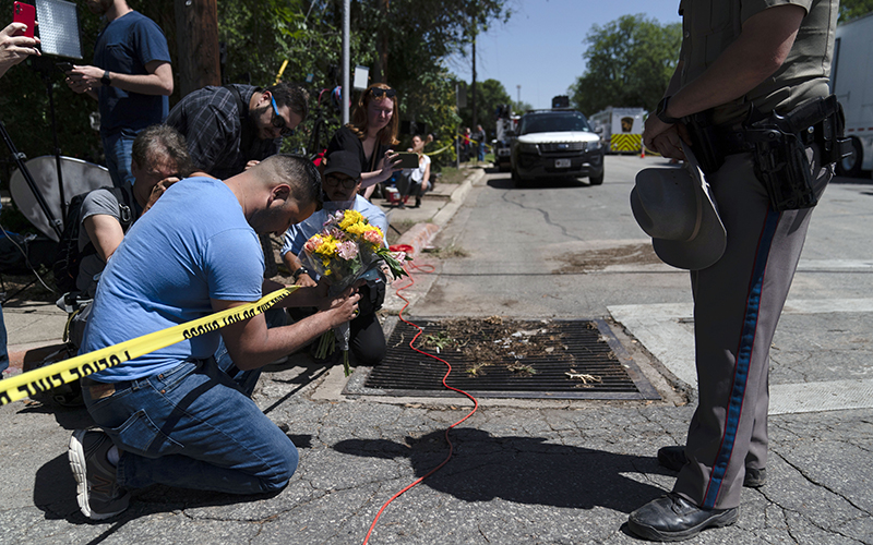 Joseph Avila, left, prays while holding flowers honoring the victims killed as an officer stands by and watches