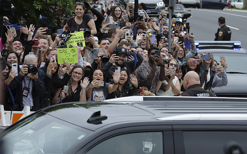 A crowd of people with signs cheer as actor Johnny Depp, traveling by car, arrives for trial