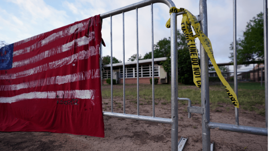 A red fabric memorial with the American flag painted on it hangs on a barricade in front of Robb Elementary School in Uvalde, Texas.