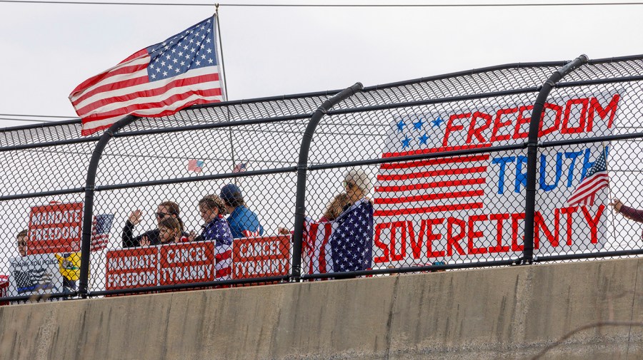 People watch a truck convoy from an overpass