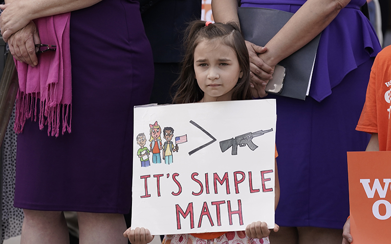 Elise Schering, 7, displays a poster with kids are greater than guns illustration, with the sign reading "It's simple math" during a National Gun Violence Awareness Day rally