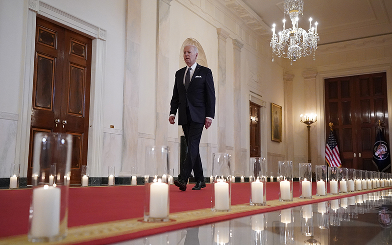 President Biden walks among rows of lit candles as he arrives from the East Room of the White House