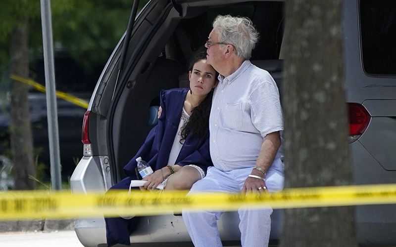 A man comforts a young woman wearing a graduation gown as they sit in the back of a car