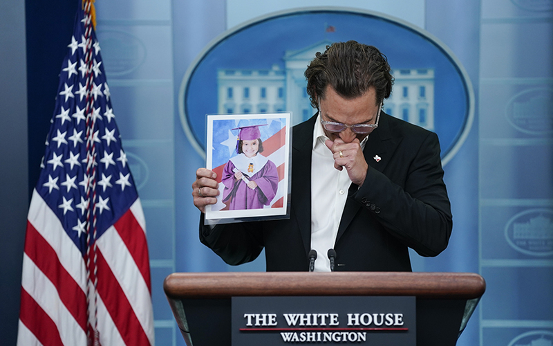 Actor Matthew McConaughey looks down as he holds an image up of Alithia Ramirez at a podium during a press briefing