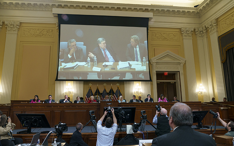 Reporters film a video deposition of former Attorney General William Barr as members of the Jan. 6 House Select Committee sit below the screen