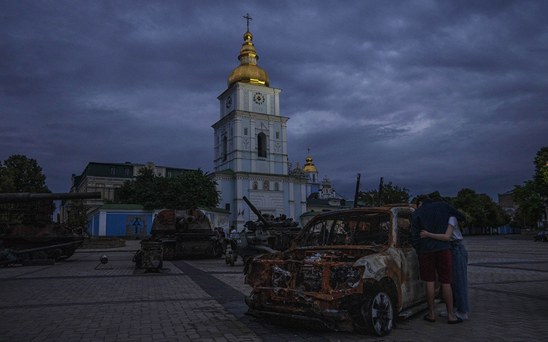 A couple look at destroyed Russian tanks installed as a symbol of war in front of St. Michael Cathedral under a dark sky