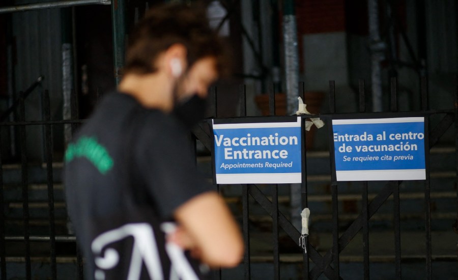 blurry image of man waiting outside, sign saying vaccination entrance in background