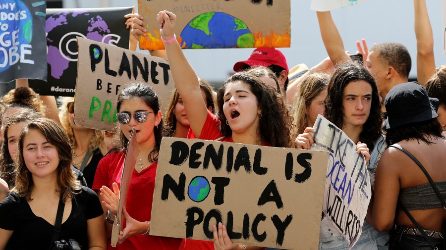 Students cheer during a climate protest, with one central sign reading, "Denial is not a policy" with an earth illustration