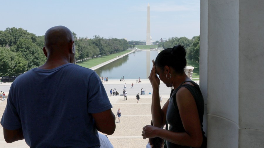 A woman wipes her forehead at the top of the stairs to the Lincoln Memorial during a heatwave in Washington, D.C.