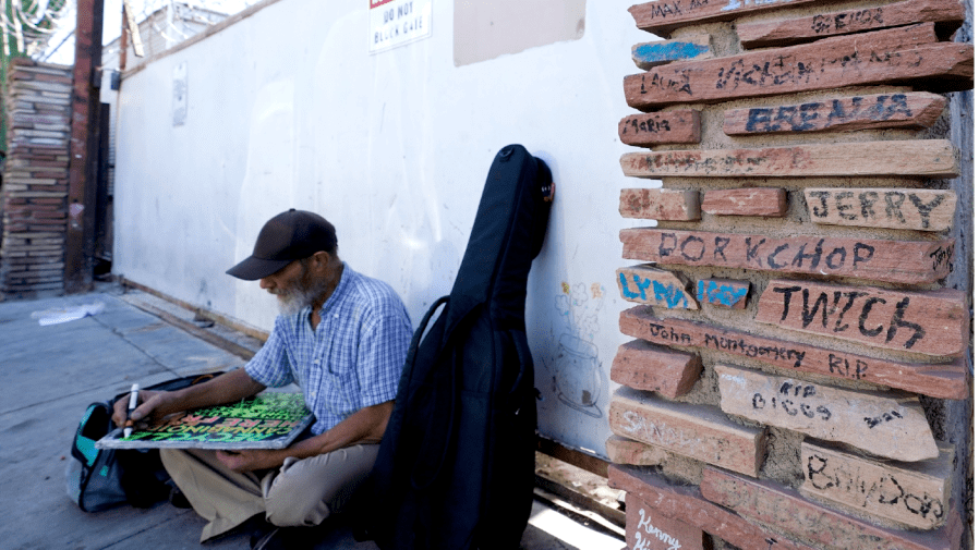 A homeless man works a sign as he sits next a monument to homeless people who have died Wednesday, April 27, 2022, in Phoenix.