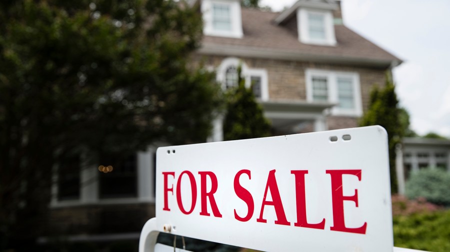 A for sale sign stands in front of a house