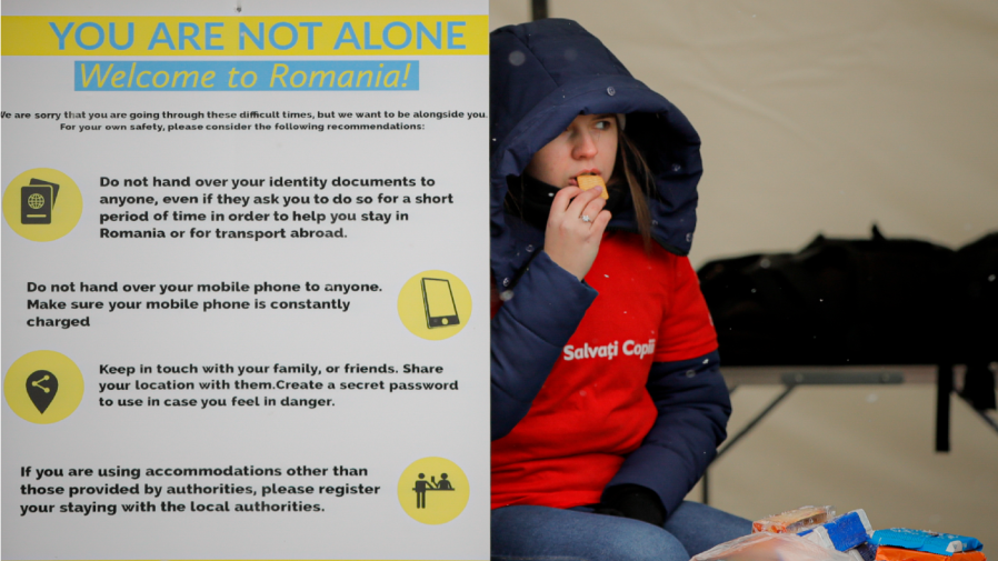 A volunteer at the international humanitarian group Save the Children sits next to a banner giving advice on personal safety at the Romanian-Ukrainian border, in Siret, Romania, Monday, March 7, 2022.