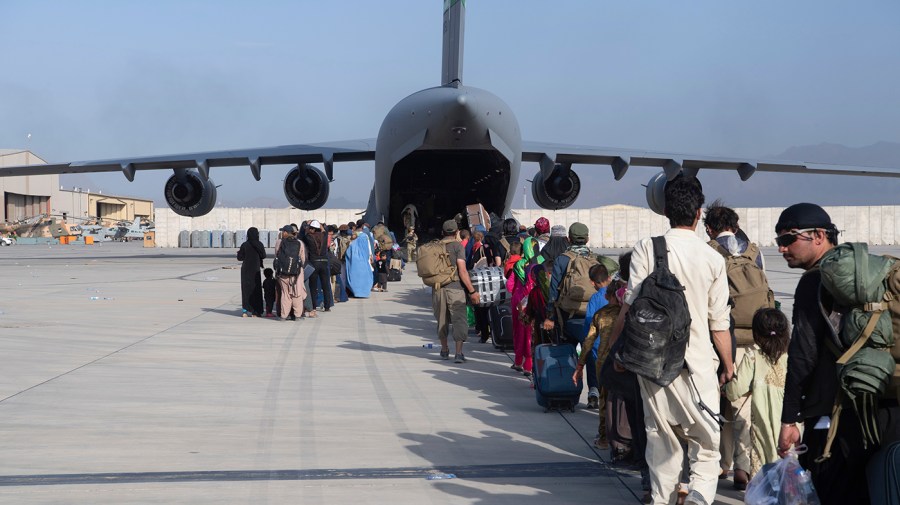 U.S. Air Force loadmasters and pilots load people being evacuated from Afghanistan onto a U.S. Air Force plane in the background as a line of people forms