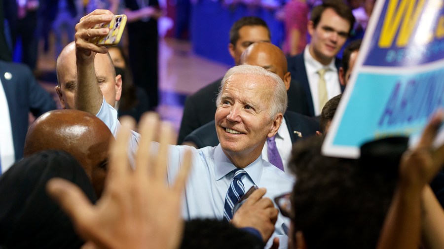 President Biden holds up a phone while taking a selfie with supporters.