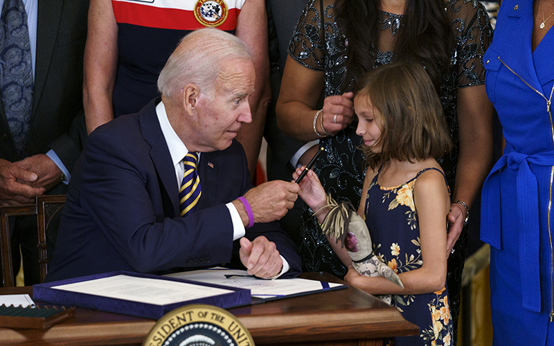 President Biden hands a pen to Brielle Robinson, daughter of the late Sgt. 1st Class Heath Robinson