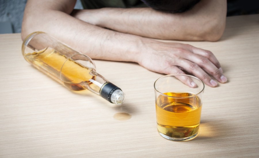 a bottle and glass of alcohol, a man's forearms resting on table