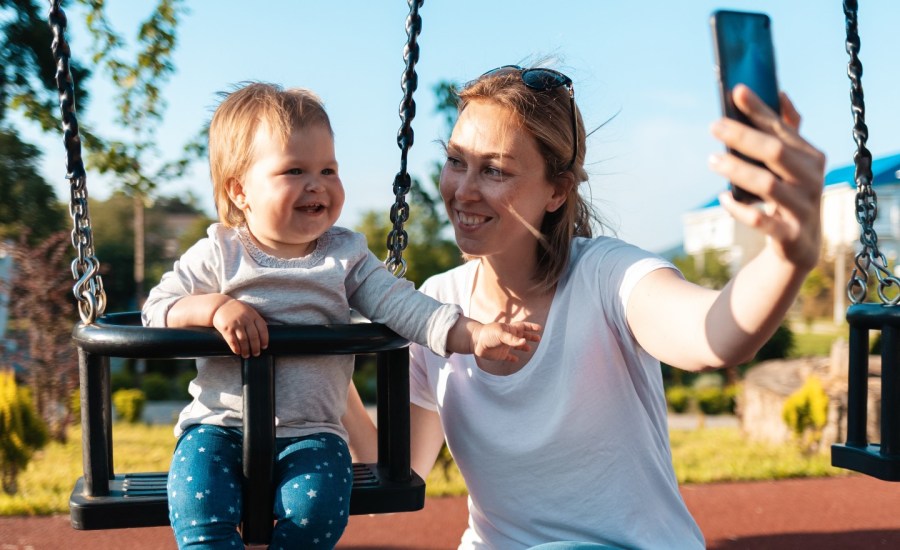 Woman takes photo of herself and baby with smart phone.