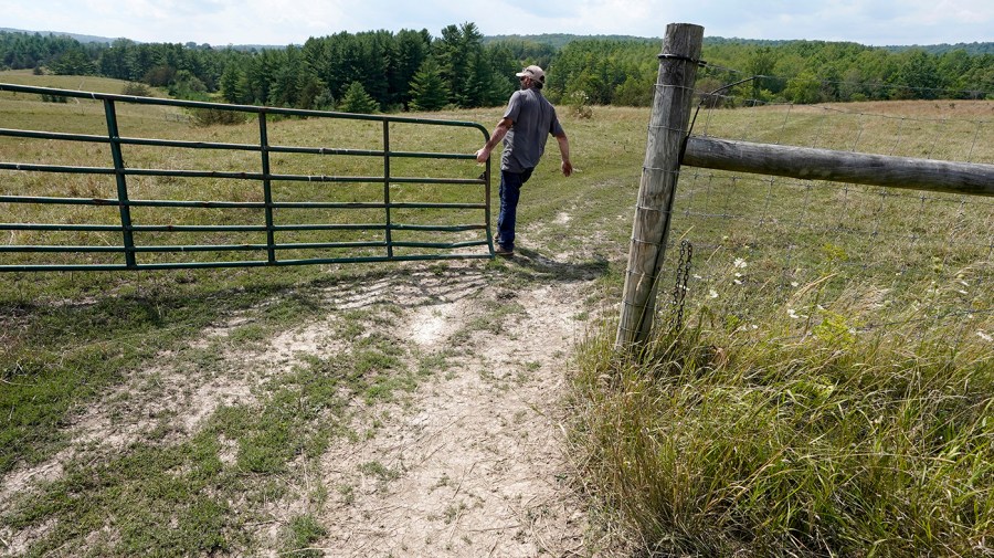 A farmer opens a gate between two fields