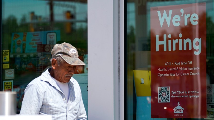 A hiring sign is displayed in a store window as a man walks past