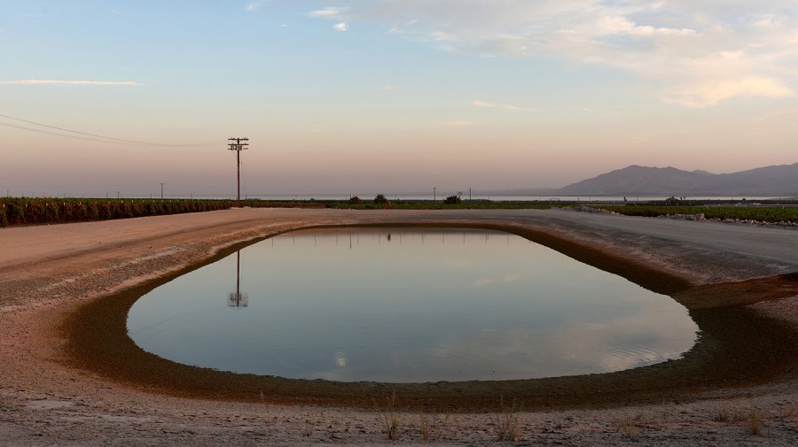 An irrigation pond is viewed near an agricultural field with the shrinking Salton Sea in the distance