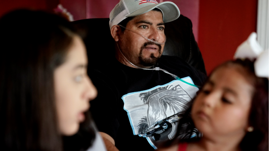 Tethered to an oxygen concentrator, Freddy Fernandez, looks on while his fiancé Vanessa Cruz, talks to their daughter Melanii, age 4, in the living room of their home Friday, June 10, 2022, in Carthage, Mo.