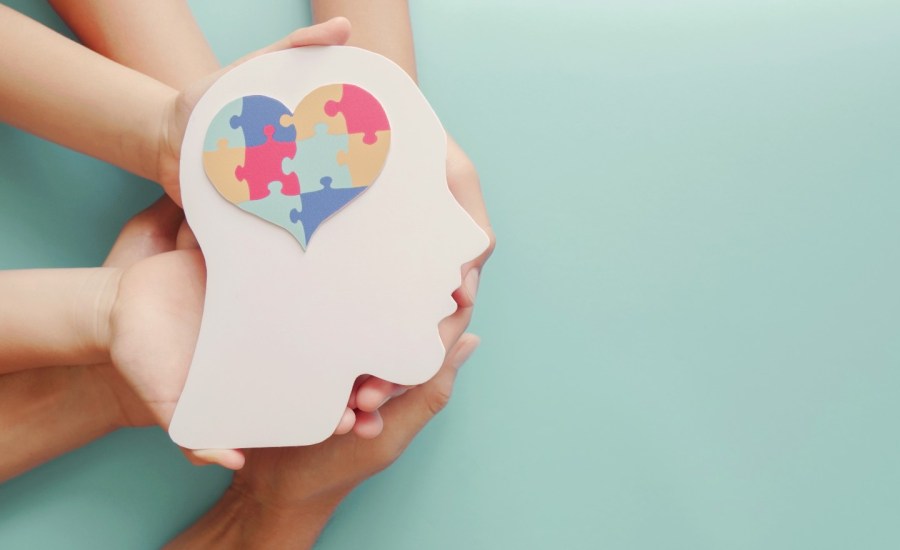 hands supporting paper cutout of head with puzzle pieces in shape of heart in brain area