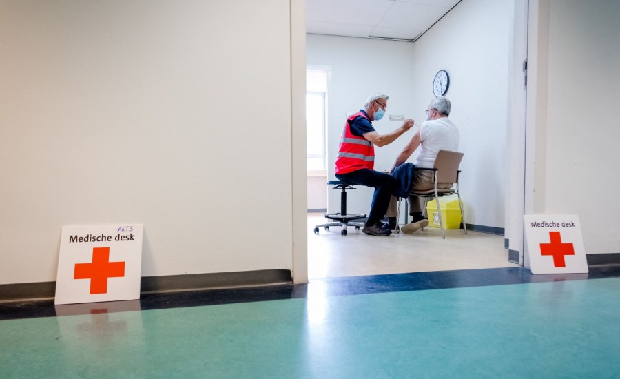 view from hallway into a room where two people are seated, one person is getting a shot in the arm