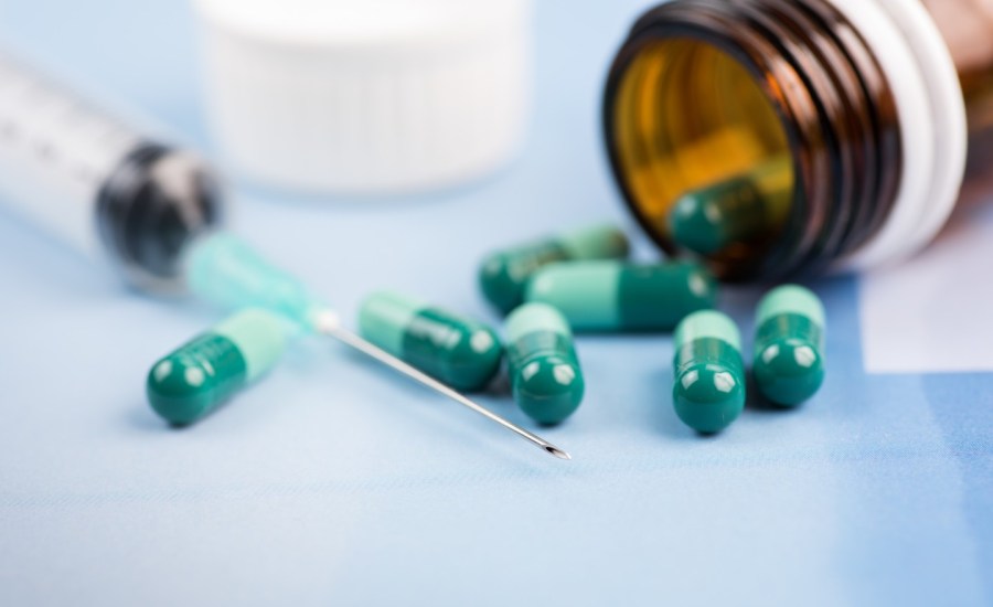 needle syringe and pills spilling out of pill bottle