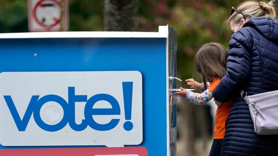 Finley Vong, 3, is held up by her mother, Tiffany Anderson, so the child can drop her mother's ballot into a drop box Wednesday, Oct. 28, 2020, in Seattle.