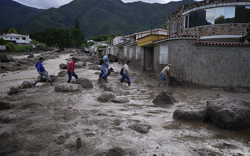 People wade through a road full of mud after the overflow of a river caused by heavy rain in El Castano, Venezuela as mountains are seen in the background