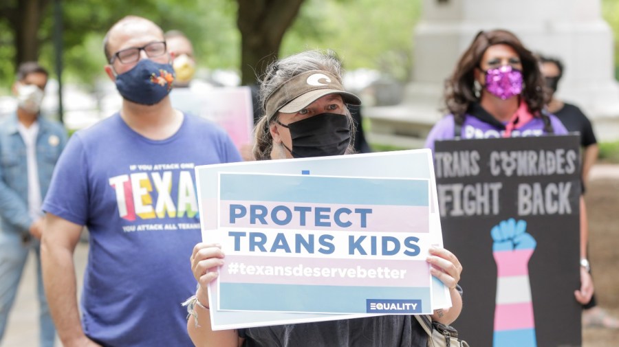 People, holding up signs like "Protect Trans Kids," participate in a protest to support trans rights.